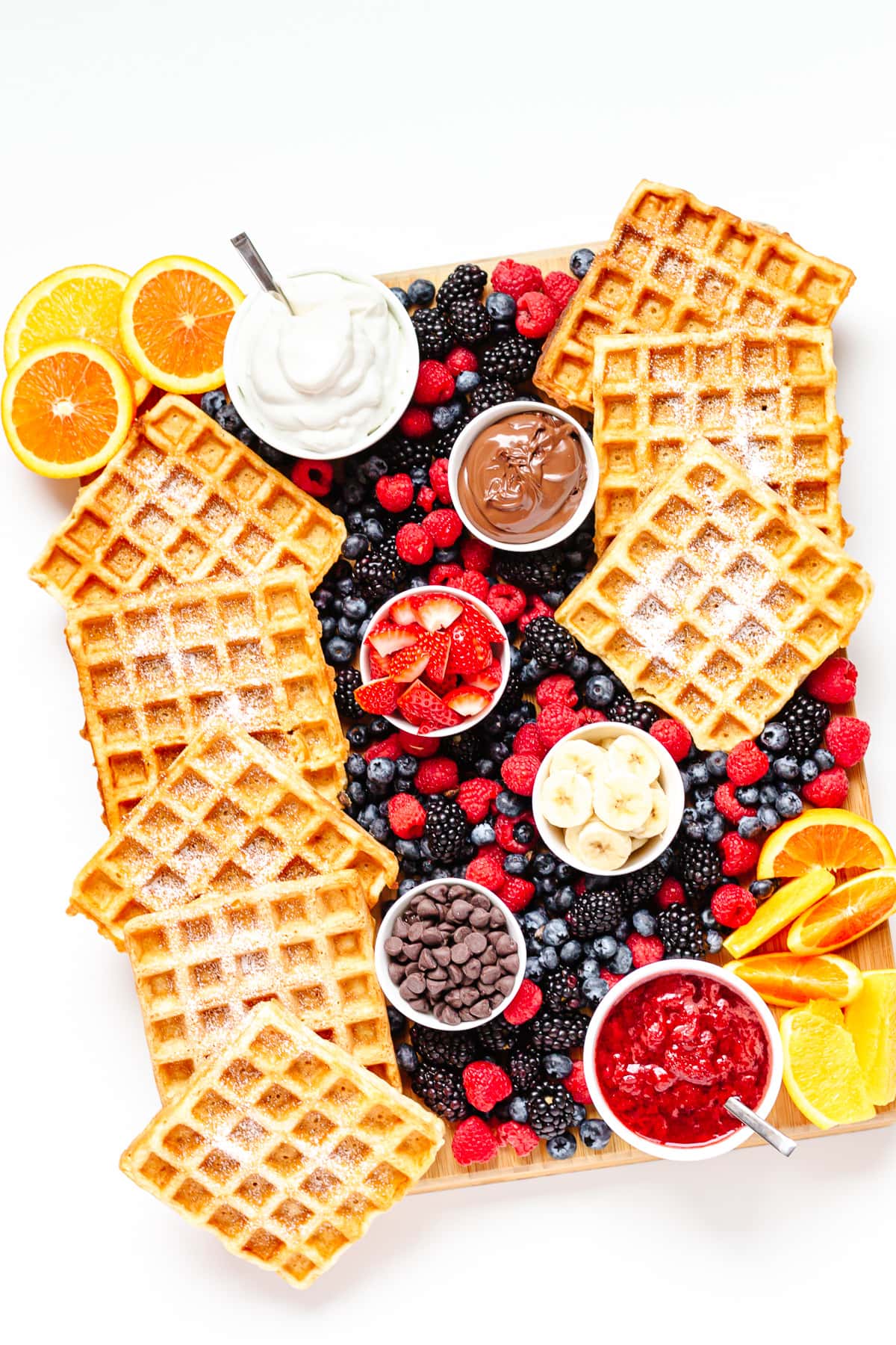 A waffle brunch board  featuring german waffles, bowls of toppings and fresh fruit.