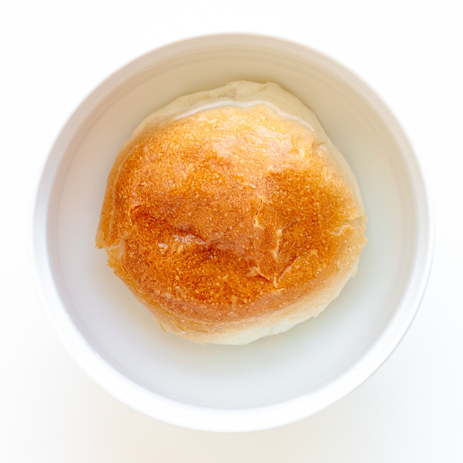 White bread roll/bun soaking in a small white bowl of water.