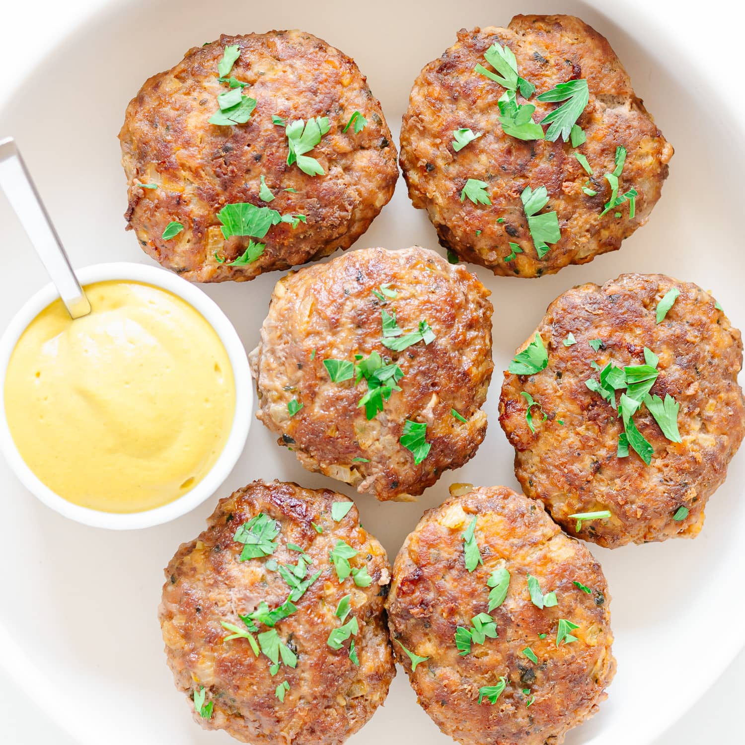 Closeup of six frikadellen garnished with chopped parsley and a small bowl of German mustard.