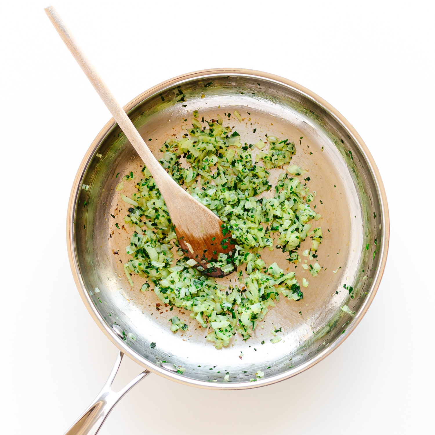 Chopped onions and parsley sautéing in a stainless steel pan. 