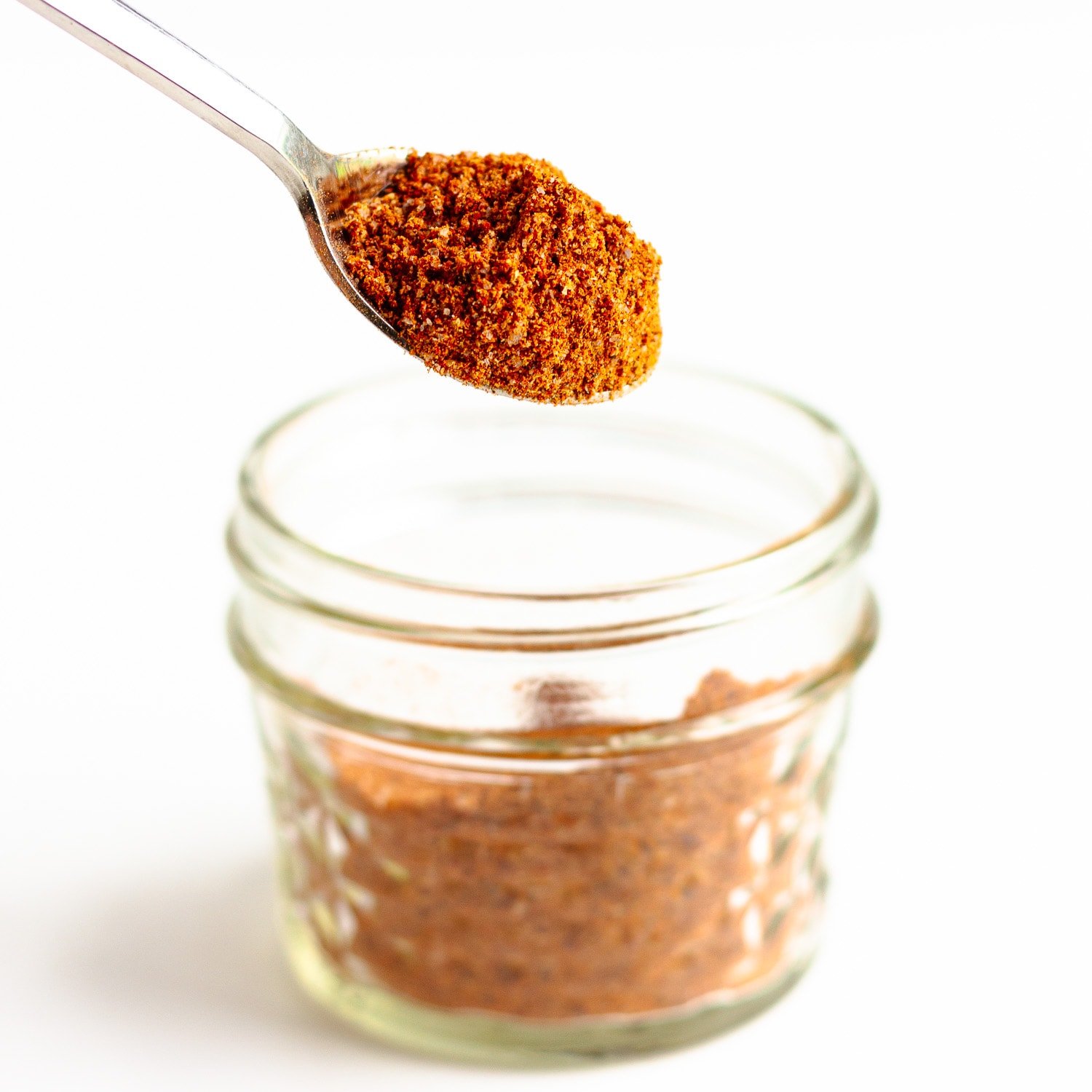 Spoon lifting fajita seasoning out of a small glass jar.