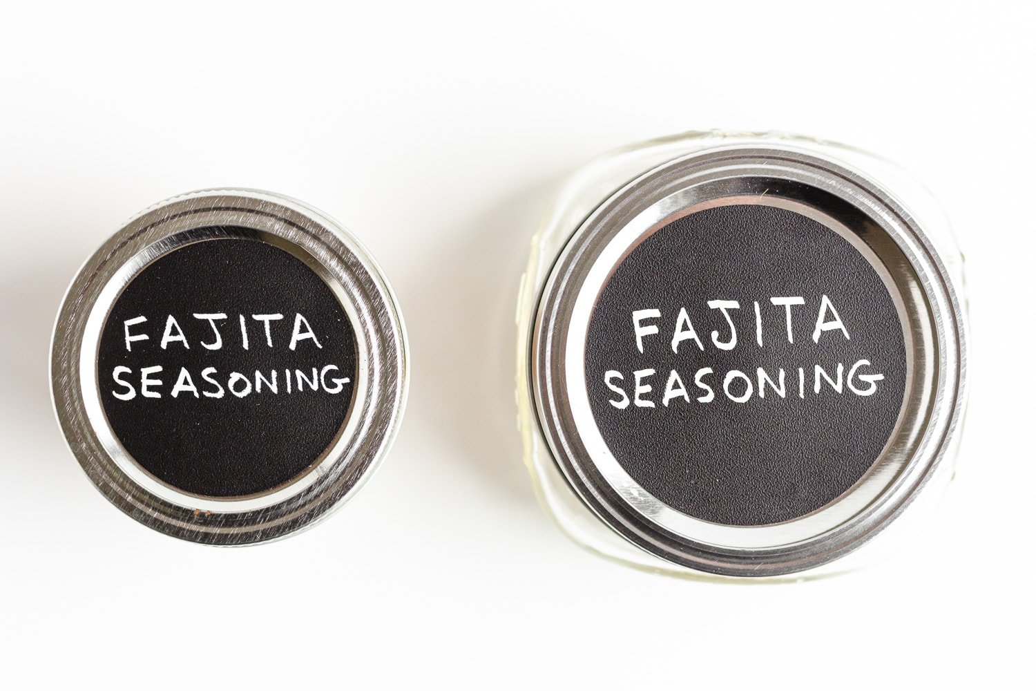 The top of of two small mason jars that have chalk labels on top with the words "Fajita Seasoning".