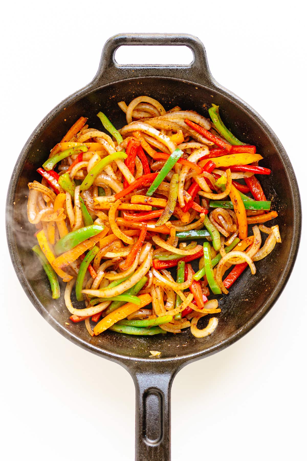 Fajita veggies in a cast iron skillet on a white background.