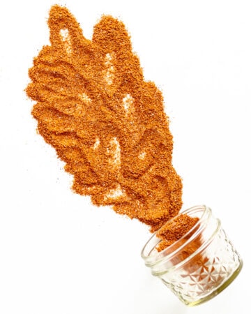 Small glass jar on its side with fajita seasoning spilling out across a white background.