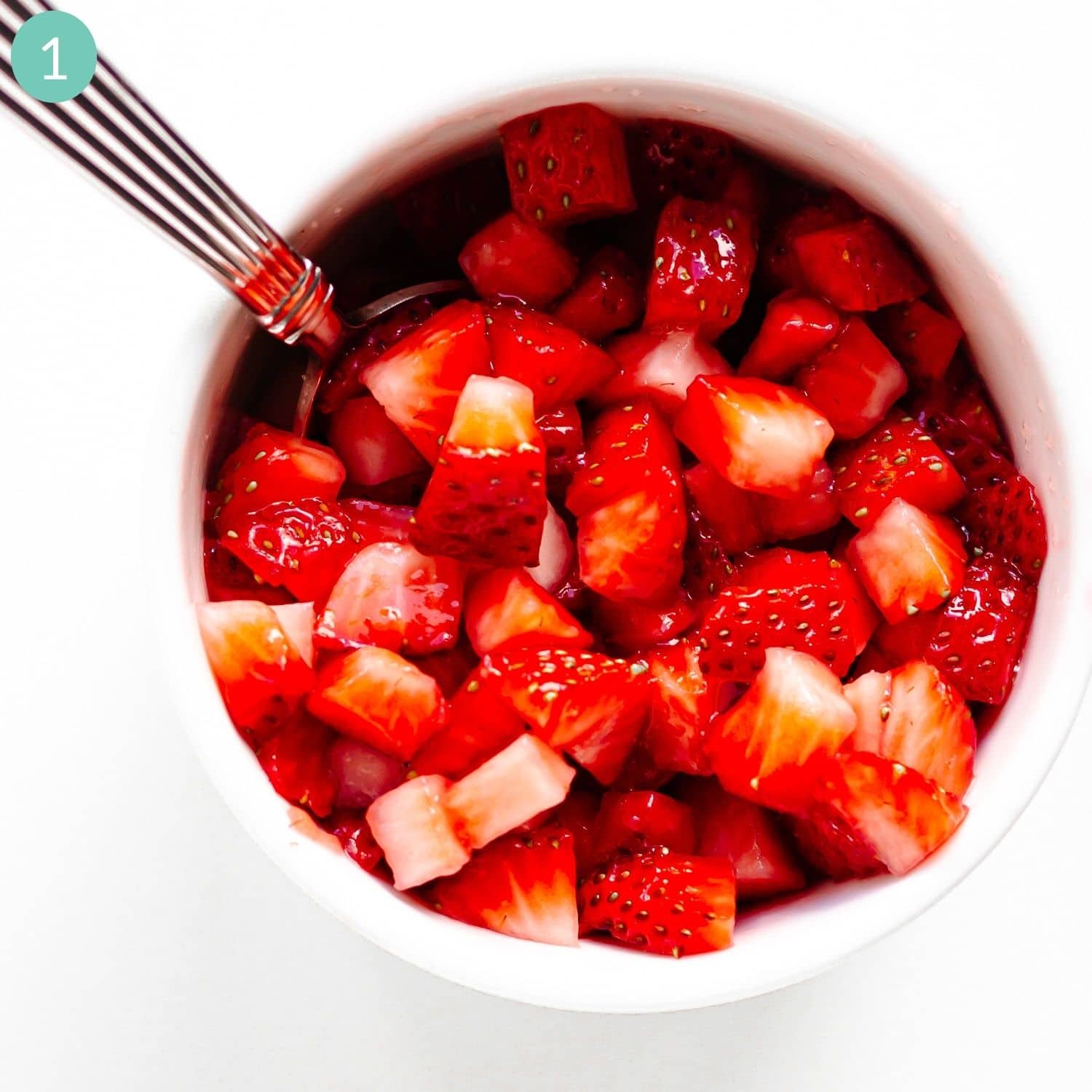 Chopped strawberries in a white bowl with spoon sticking out.