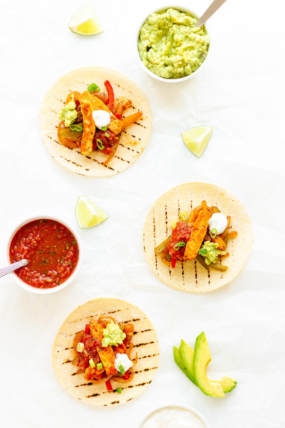 Three halloumi fajitas on a white background with various toppings laid out around them.