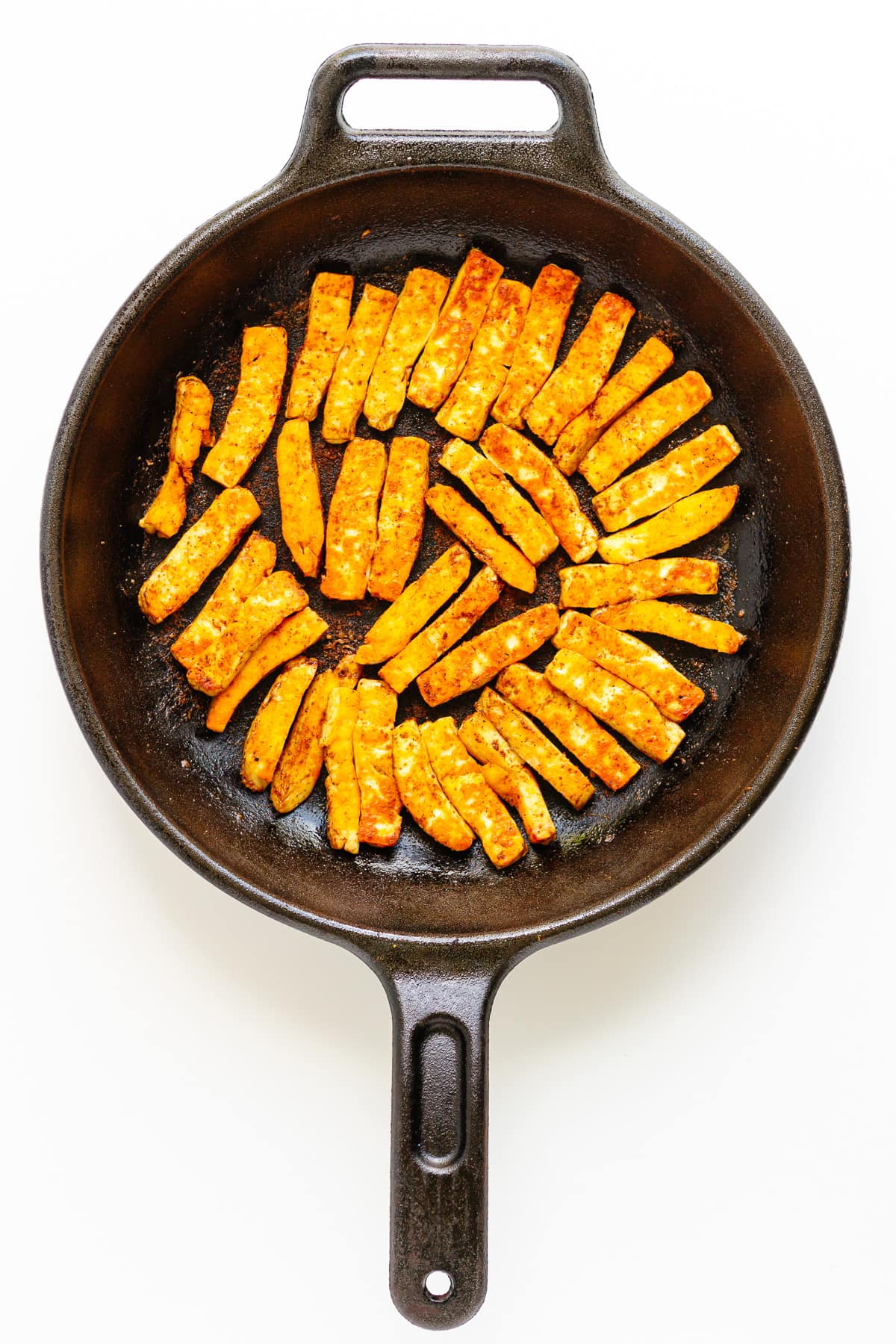 Fried halloumi strips in a cast iron skillet.