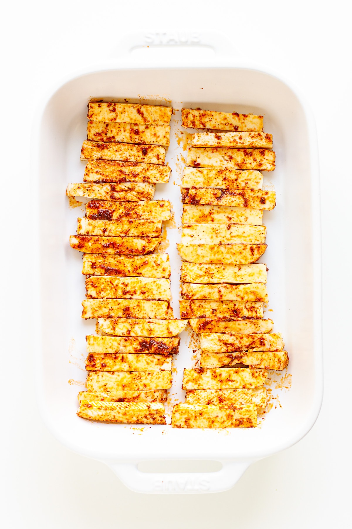 Seasoned halloumi strips in a white casserole dish.