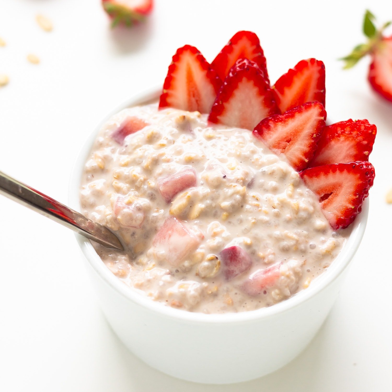 Strawberry overnight oats in a small white bowl with spoon and garnished with strawberry slices.