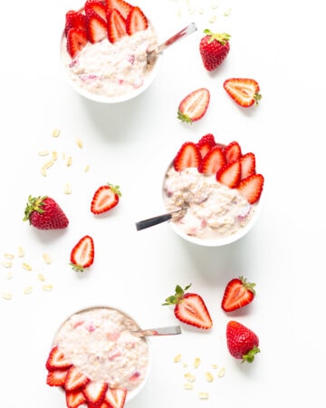 Overhead view of three bowls of strawberry overnight oats garnished with strawberry slices.