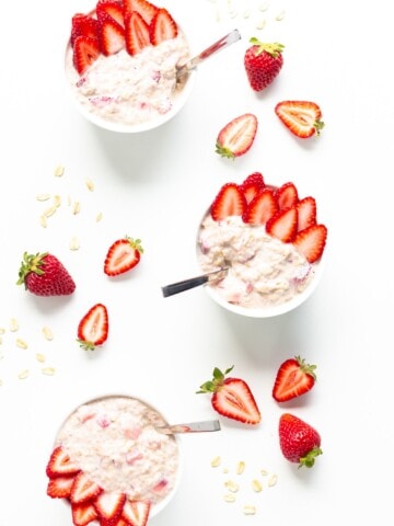 Overhead view of three bowls of strawberry overnight oats garnished with strawberry slices.