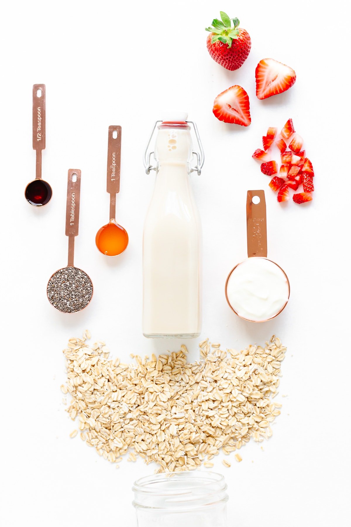 Ingredients needed to make strawberry overnight oats arranged on a white background.