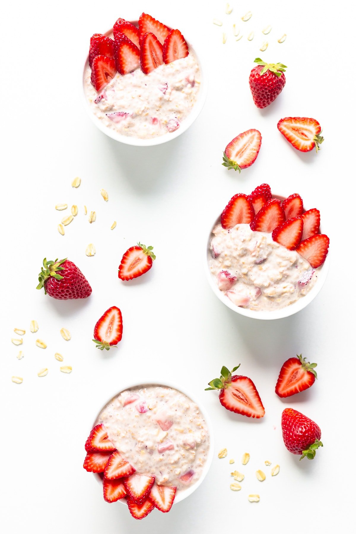 Three small bowls of strawberry overnight oats garnished with fresh strawberry slices.