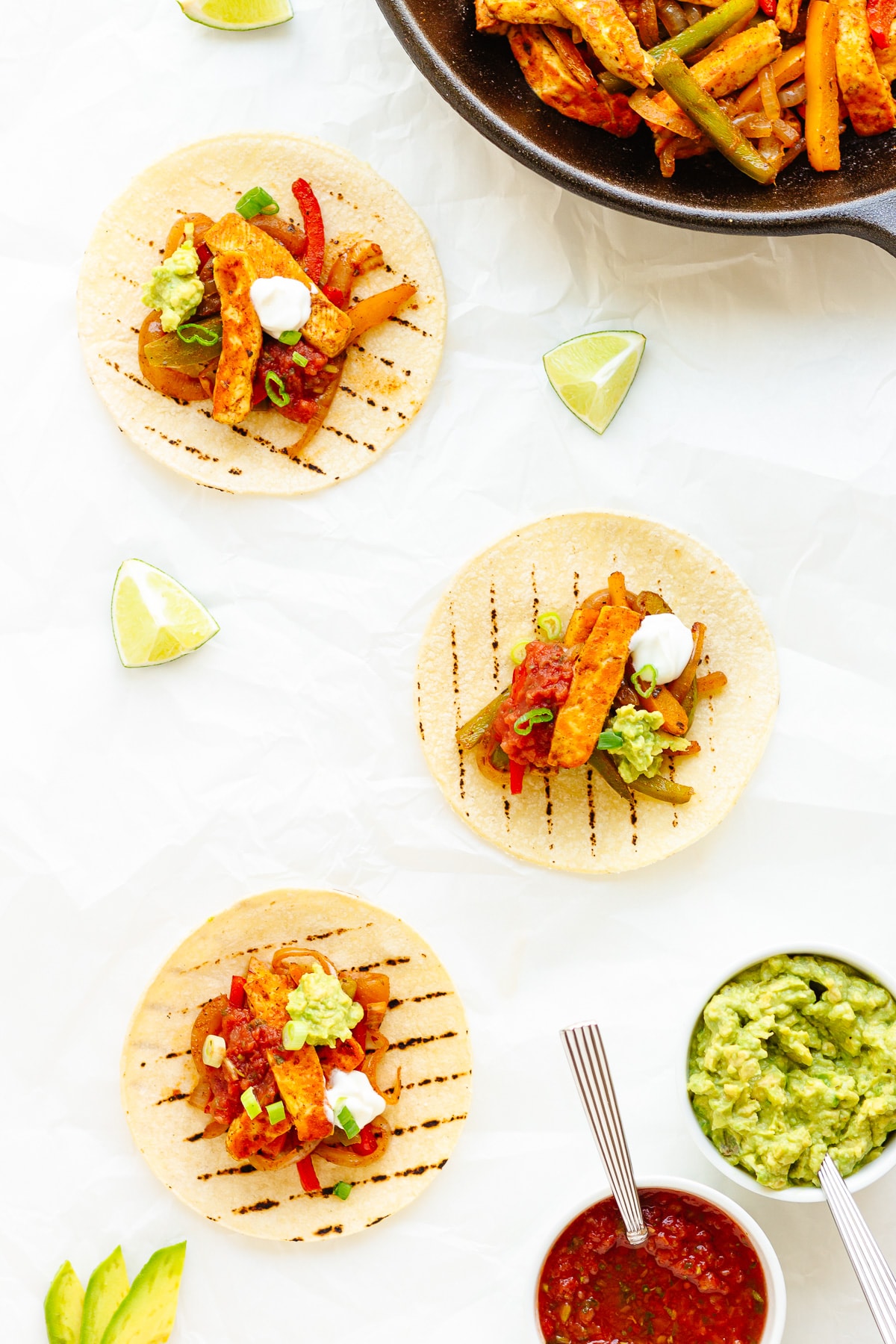 Three topped halloumi vegetable fajitas with a skillet of the mixture and toppings around them.