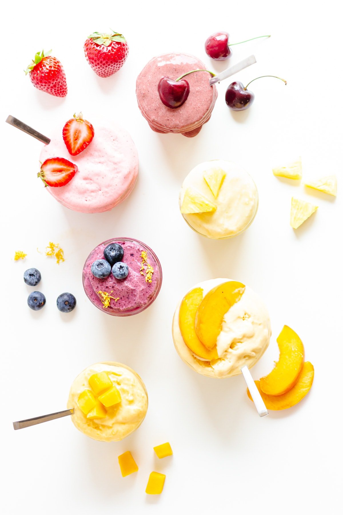 Overhead photo of six different flavors of blender ice cream in jars with fruit scattered around.