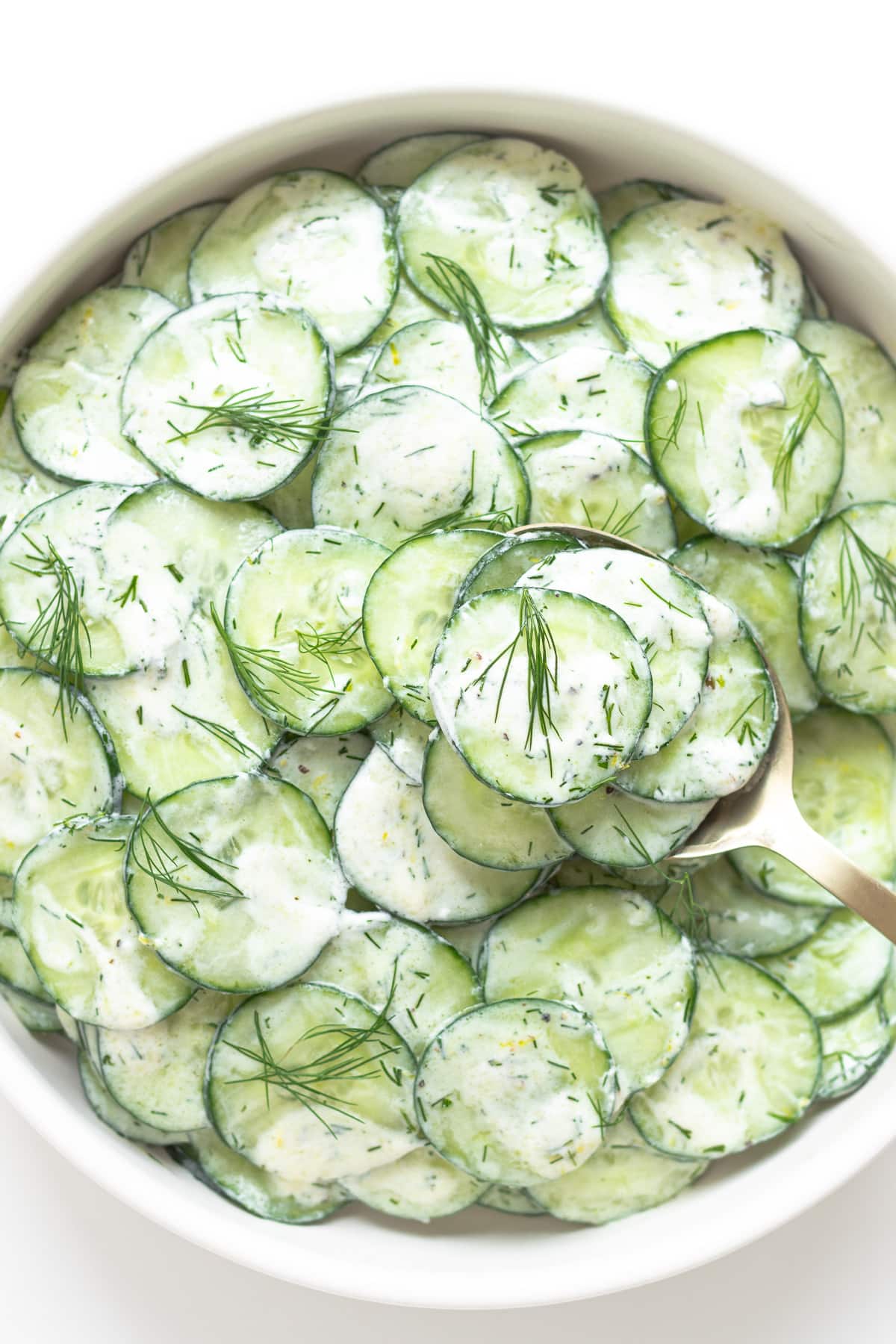 Serving spoon lifting some cucumber salad out of bowl.