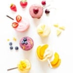 Overhead image of six different flavors of blender ice cream in jars with fruit garnishes.