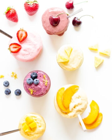 Overhead image of six different flavors of blender ice cream in jars with fruit garnishes.
