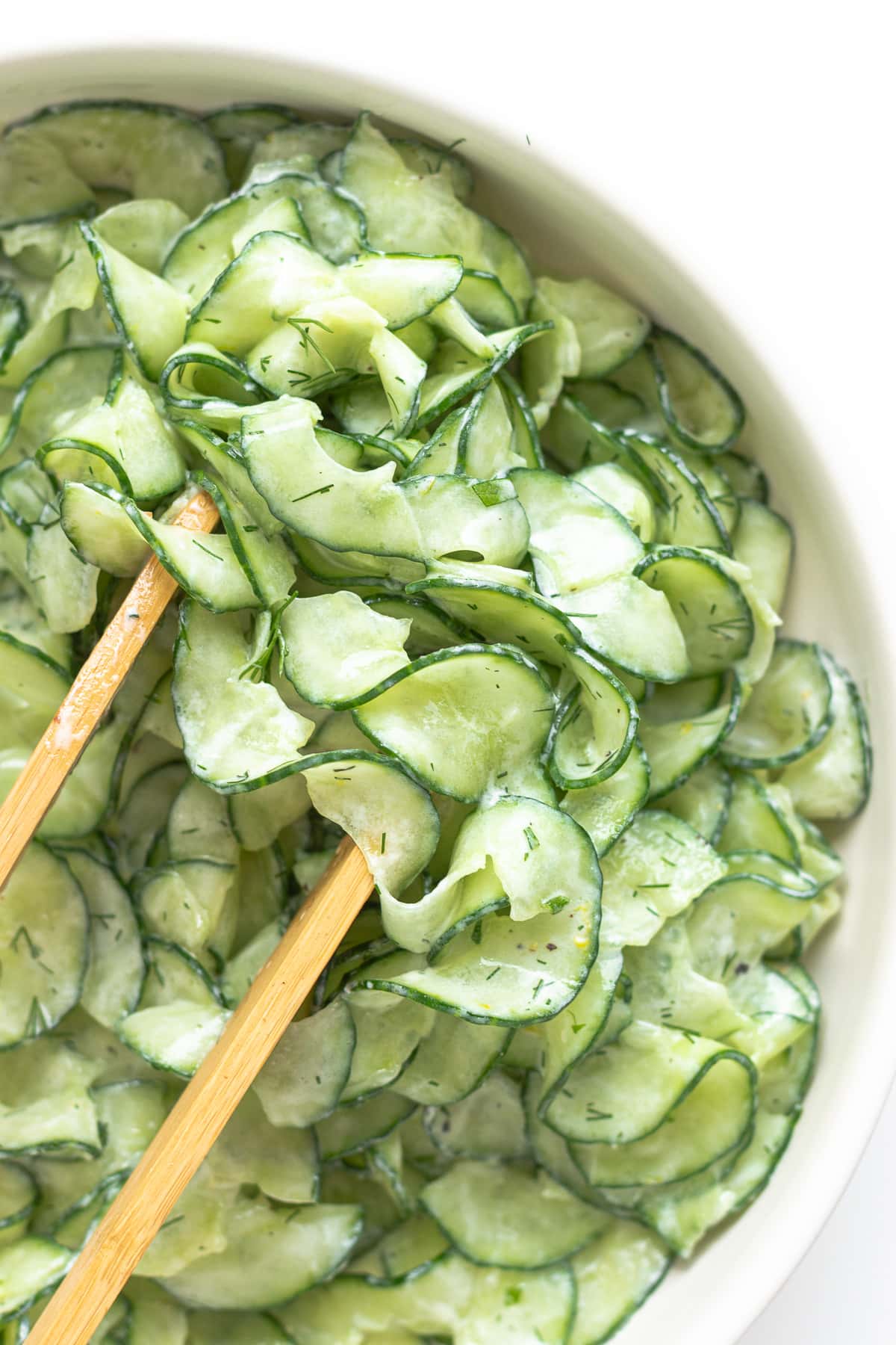 Bowl of spiralized cucumber salad with wood tongs.