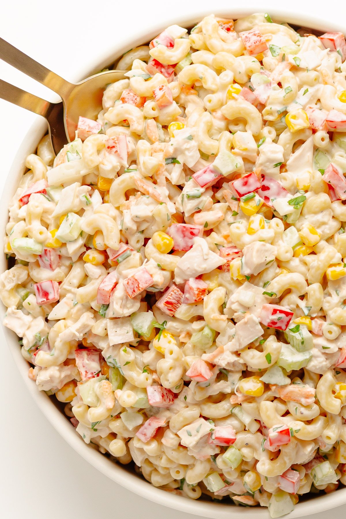 Chicken macaroni pasta salad in a white serving bowl with serving spoons.