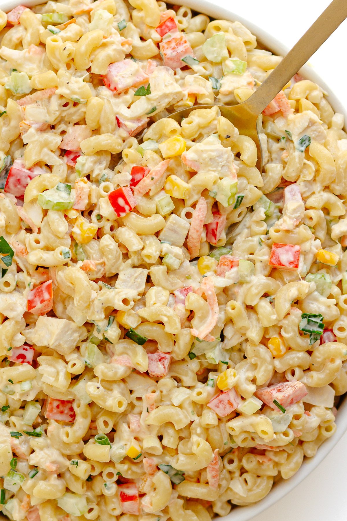 Creamy chicken macaroni salad in a white serving bowl with gold serving spoon.