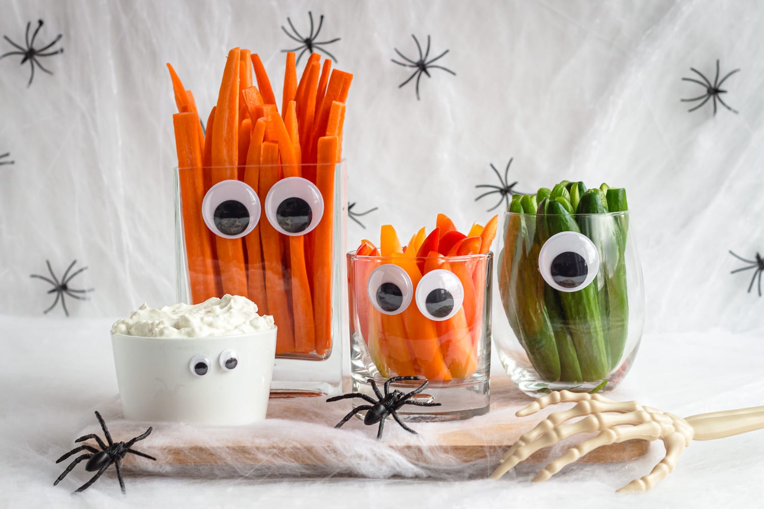 Simple Halloween veggie tray featuring carrots, peppers, cucumber and dip in glassware with googly eyes.