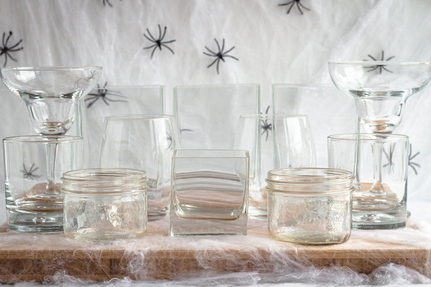 Variety of glassware set on a wooden board surrounded by fake cobwebs and spiders.