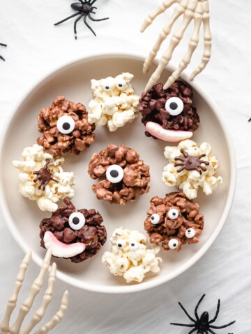 Serving bowl of chocolate Halloween popcorn balls with skeleton hands reaching in.