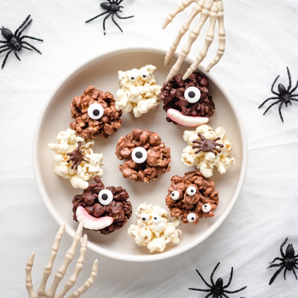 Serving bowl of chocolate Halloween popcorn balls with skeleton hands reaching in.