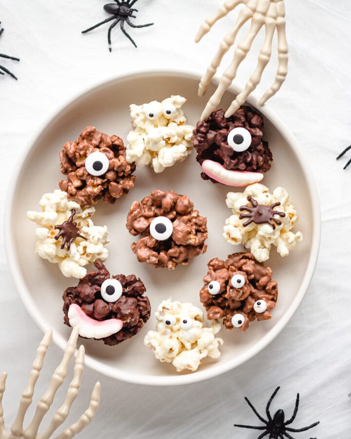 Serving bowl of chocolate Halloween popcorn balls with skeleton hands reaching in.