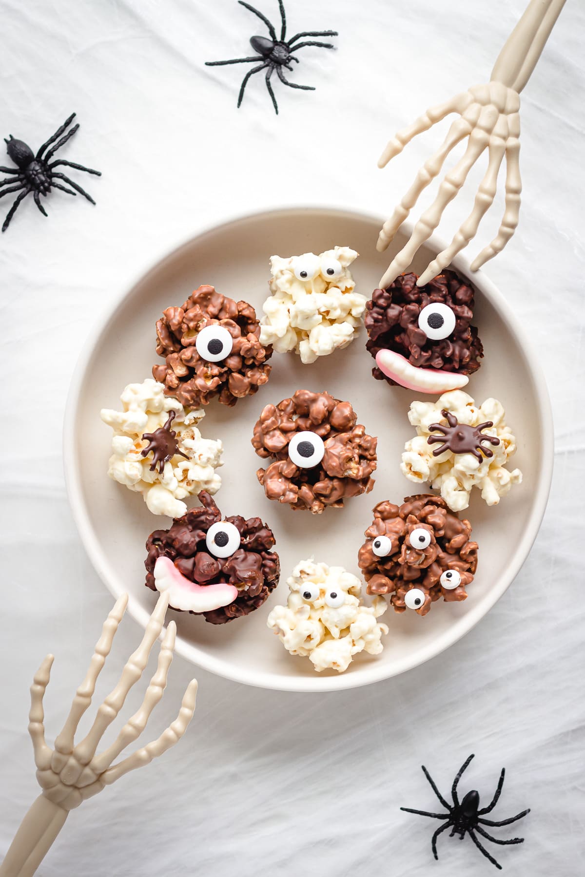 Bowl of Halloween chocolate popcorn balls with skeleton hands reaching in and fake spiders around the bowl.