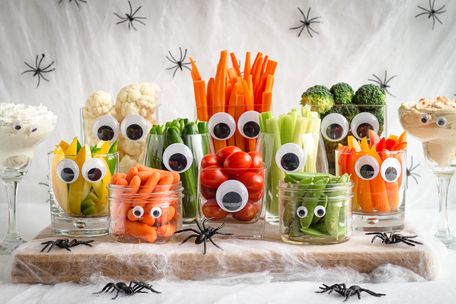 Large Halloween themed veggie tray made using glassware and googly eyes surrounded by fake spiders and cobwebs.