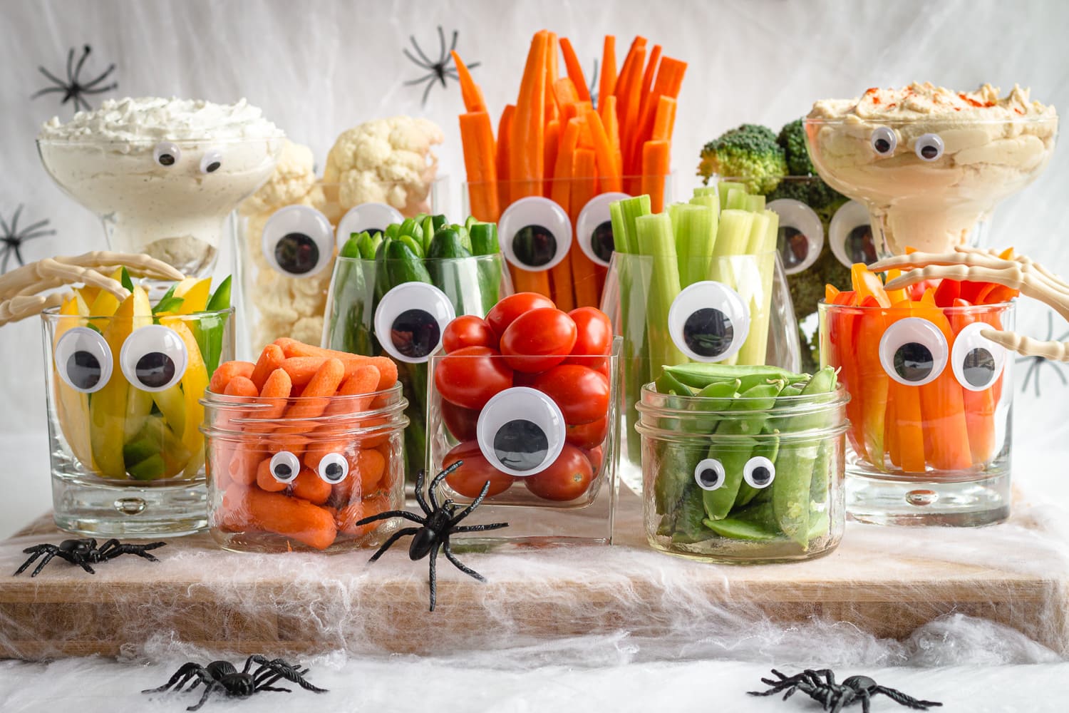A Halloween veggie tray featuring "monsters" made from glassware with googly eyes which are then filled with a variety of different veggies and dip.