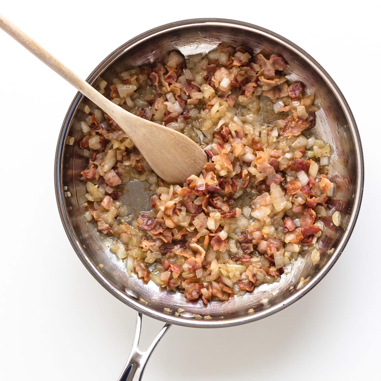 Sautéed bacon and onions in a stainless steel frying pan. 