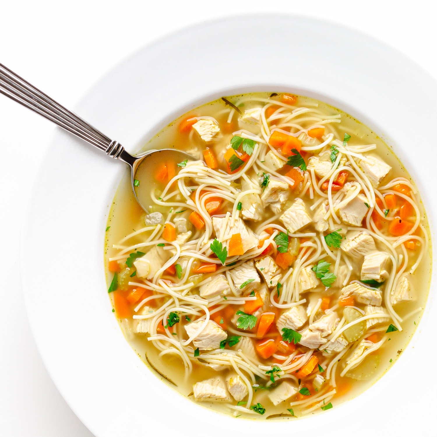 White bowl of turkey noodle soup with spoon.