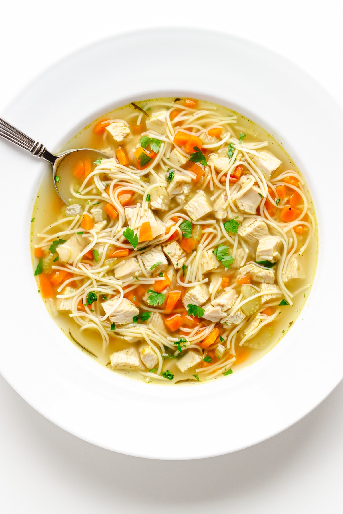 White bowl of turkey noodle soup with spoon.