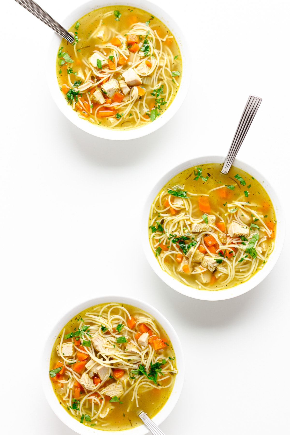 Three bowls of turkey noodle soup on a white background.