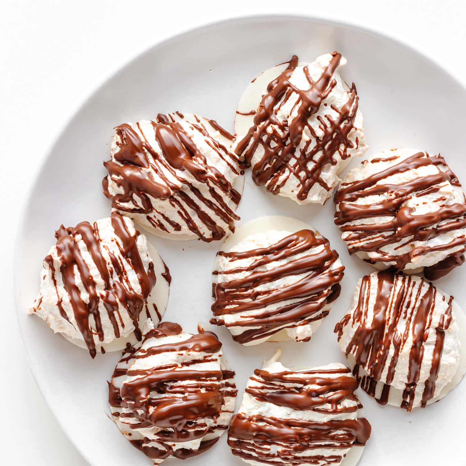 Chocolate drizzled coconut macaroons on a white plate.