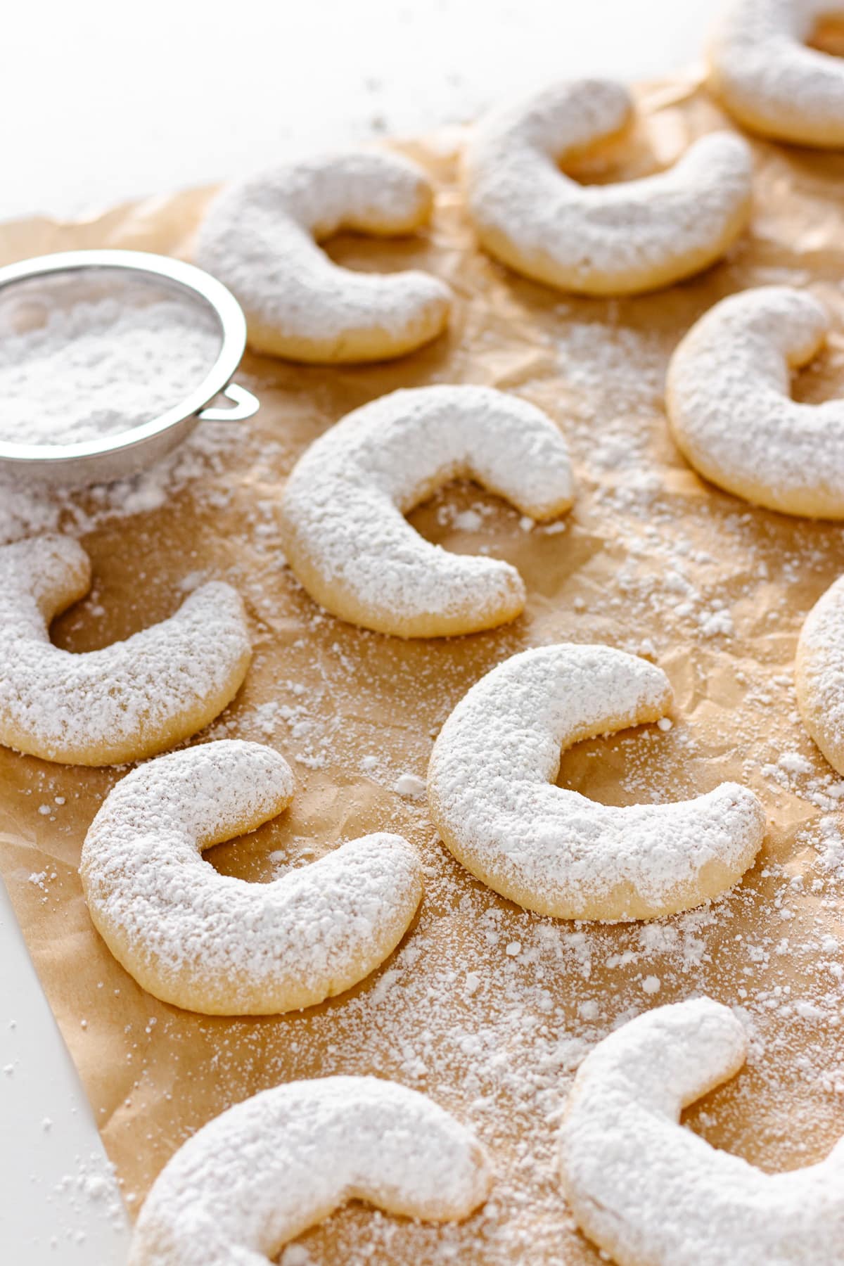 Powdered sugar dusted crescent cookies on a sheet of parchment paper.
