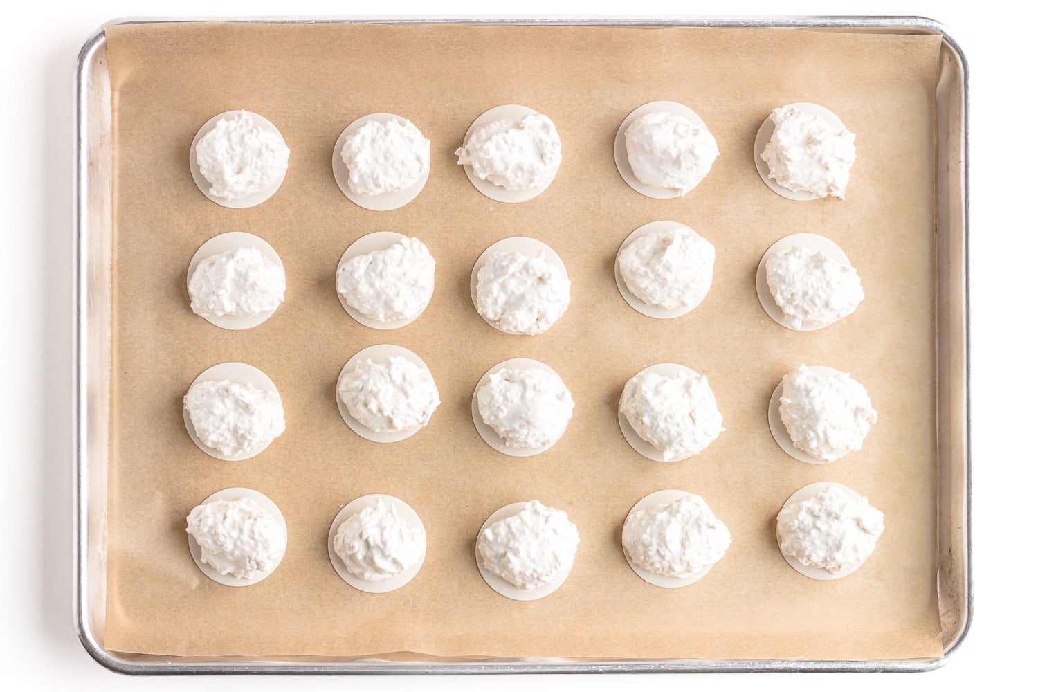 Scoops of coconut meringue macaroon mixture on top of oblaten on a parchment paper lined baking sheet.