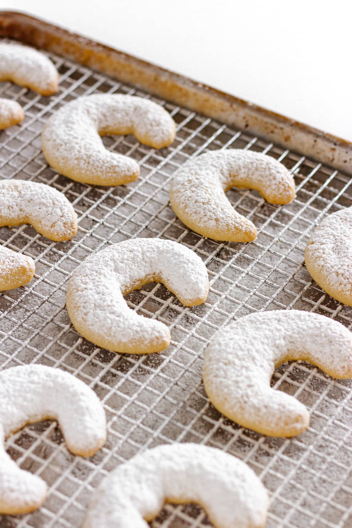 Crescent cookies dusted with powdered sugar on a cooling rack.