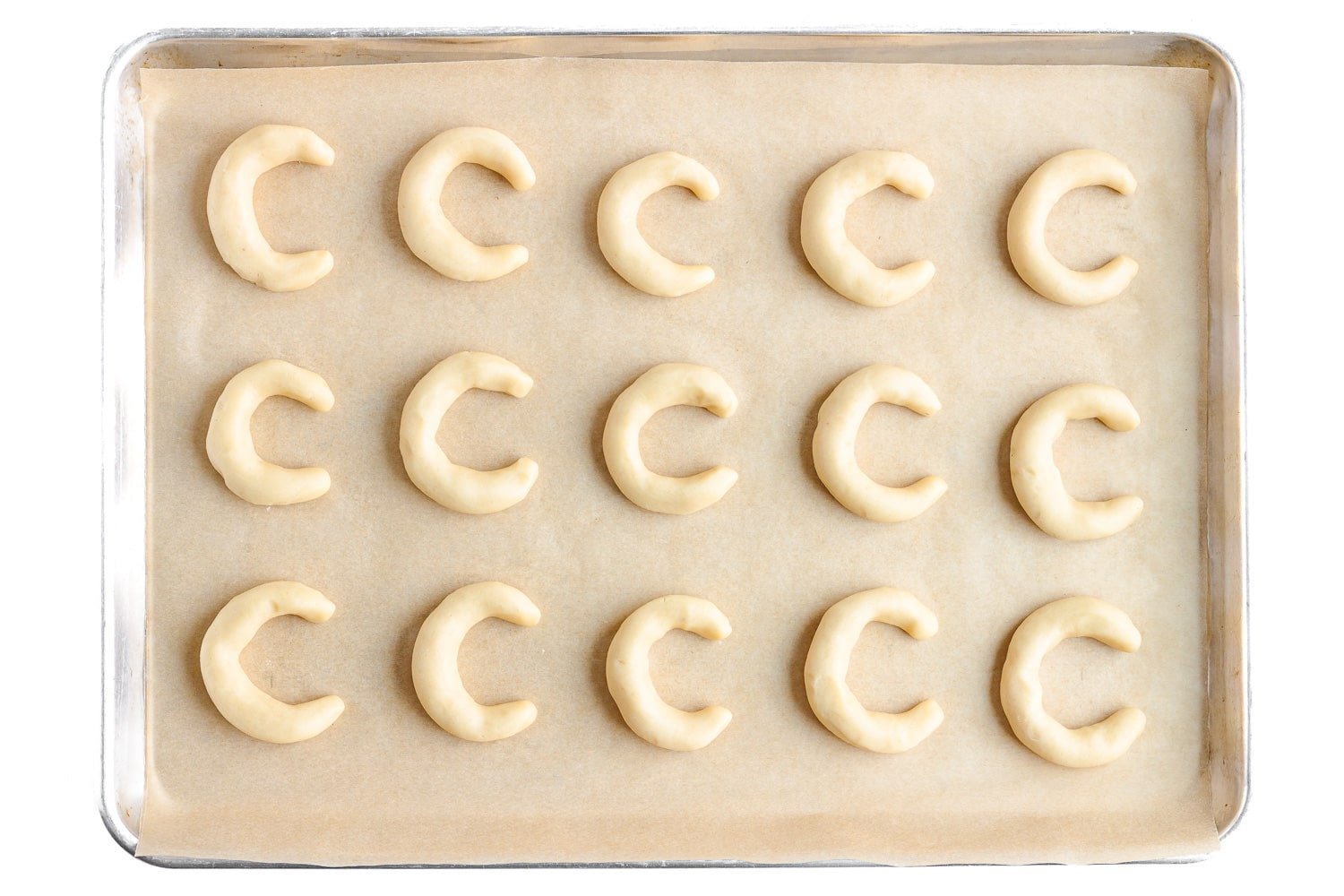 Unbaked crescent shaped cookies on a parchment paper lined baking sheet.