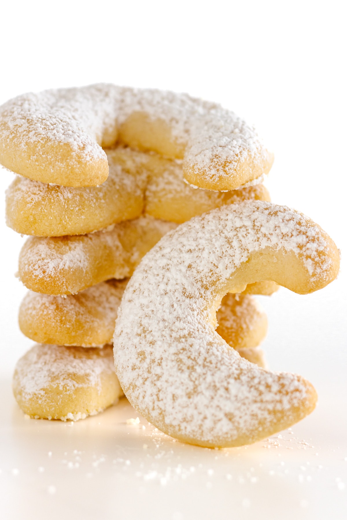 Stack of vanilla almond crescent cookies with one cookie leaning against the stack.