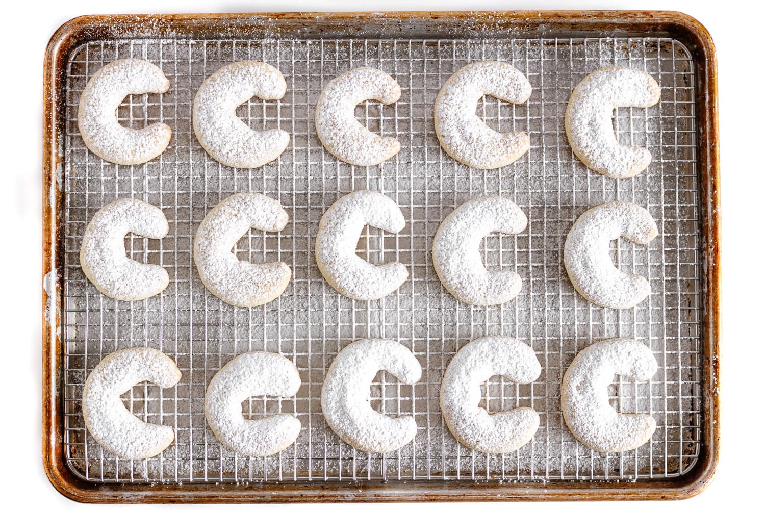 Vanillekipferl dusted with powdered sugar on a baking sheet fitted with a wire rack.