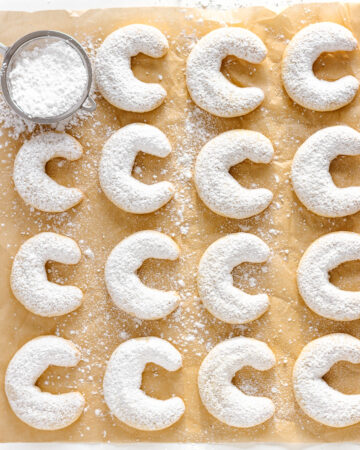 Vanillekipferln (vanilla almond crescent cookies) dusted with powdered sugar and lined up on a square piece of parchment paper.