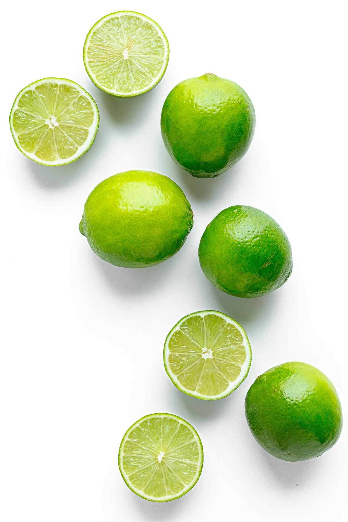 A bunch of whole and halved limes arranged across a white background.