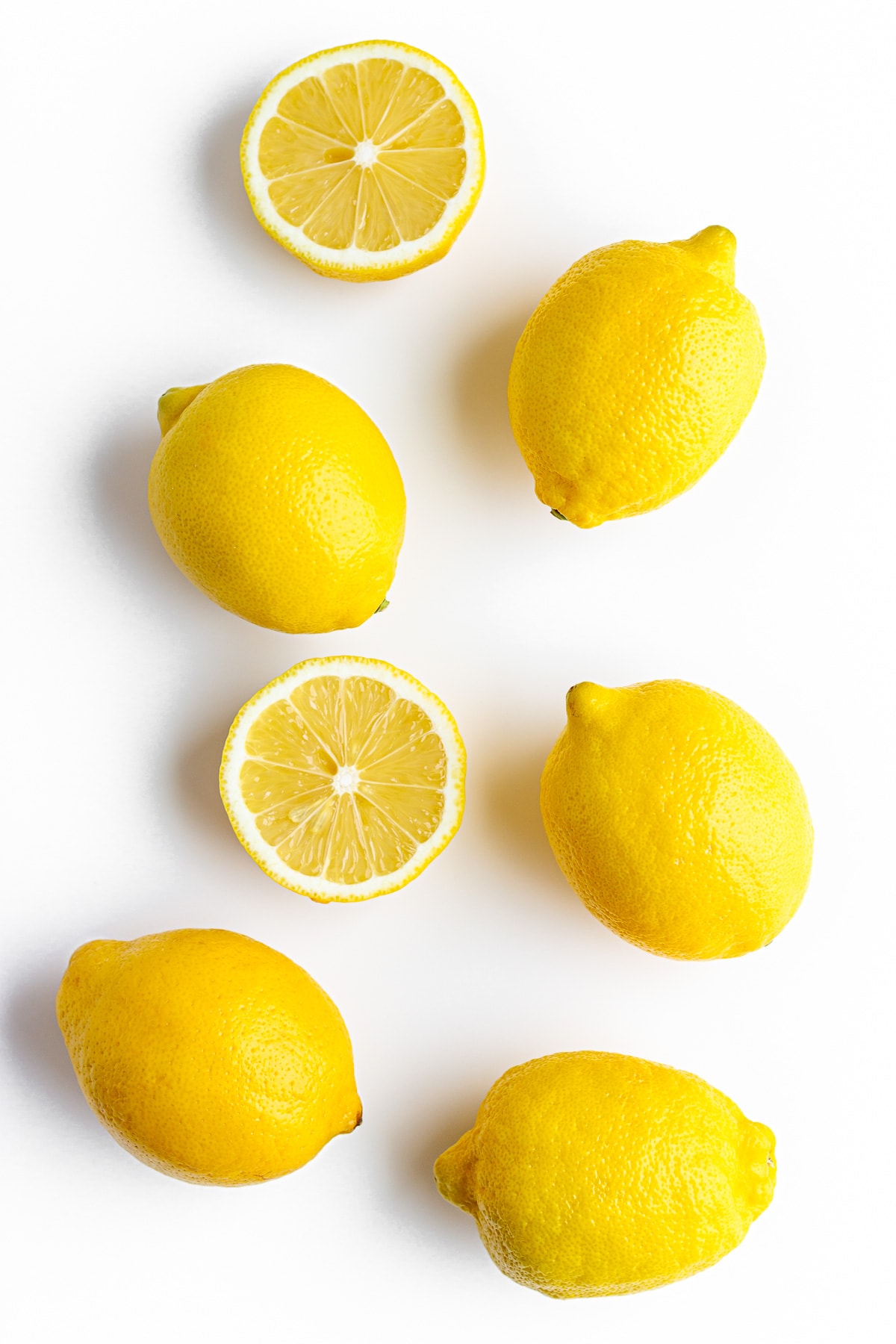 Bunch of whole and halved lemons arranged on a white background.