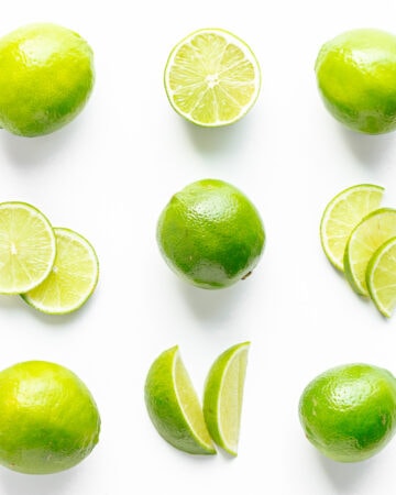 Flat lay of limes cut in a variety of different ways on a white background.