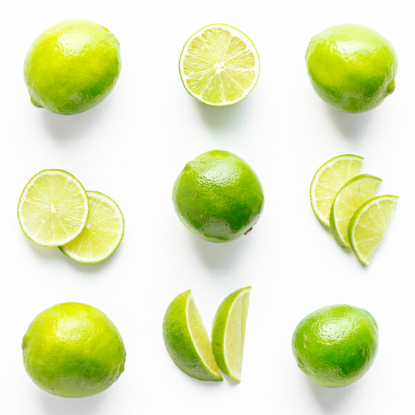 Flat lay of limes cut in a variety of different ways on a white background.