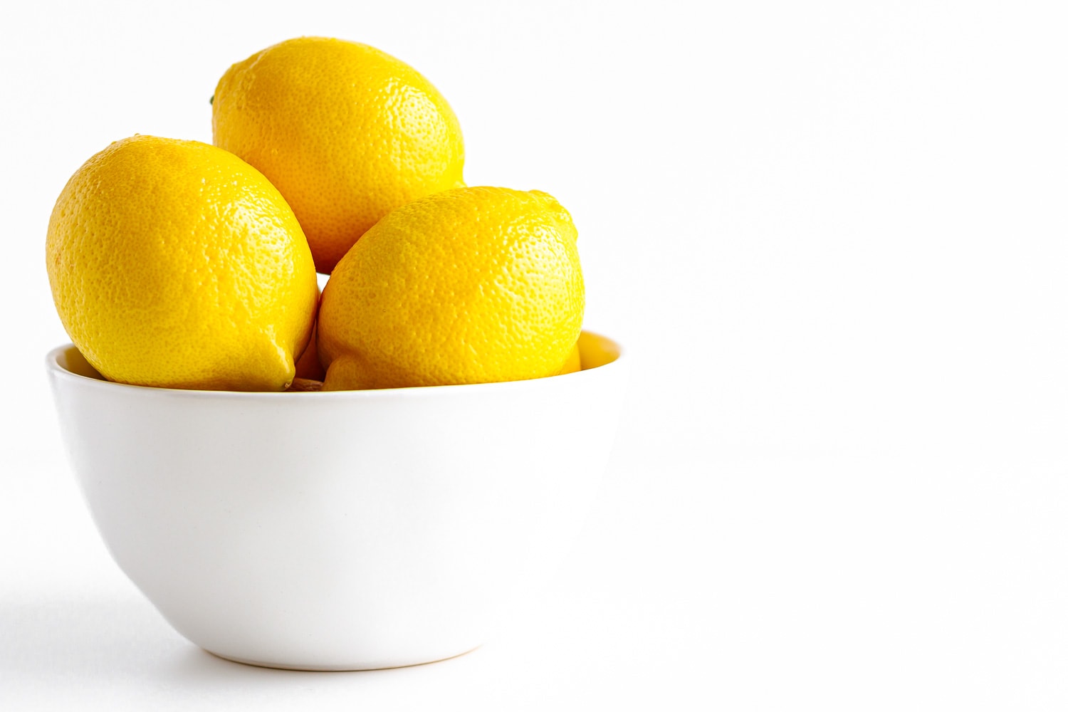 Lemons in a white bowl against a white backdrop.